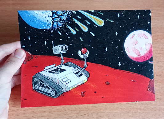 Hand holding a A5 Print of a Mars exploration robot looking intently at a small rock while a planet explodes in the background raining down a shower of meteors.