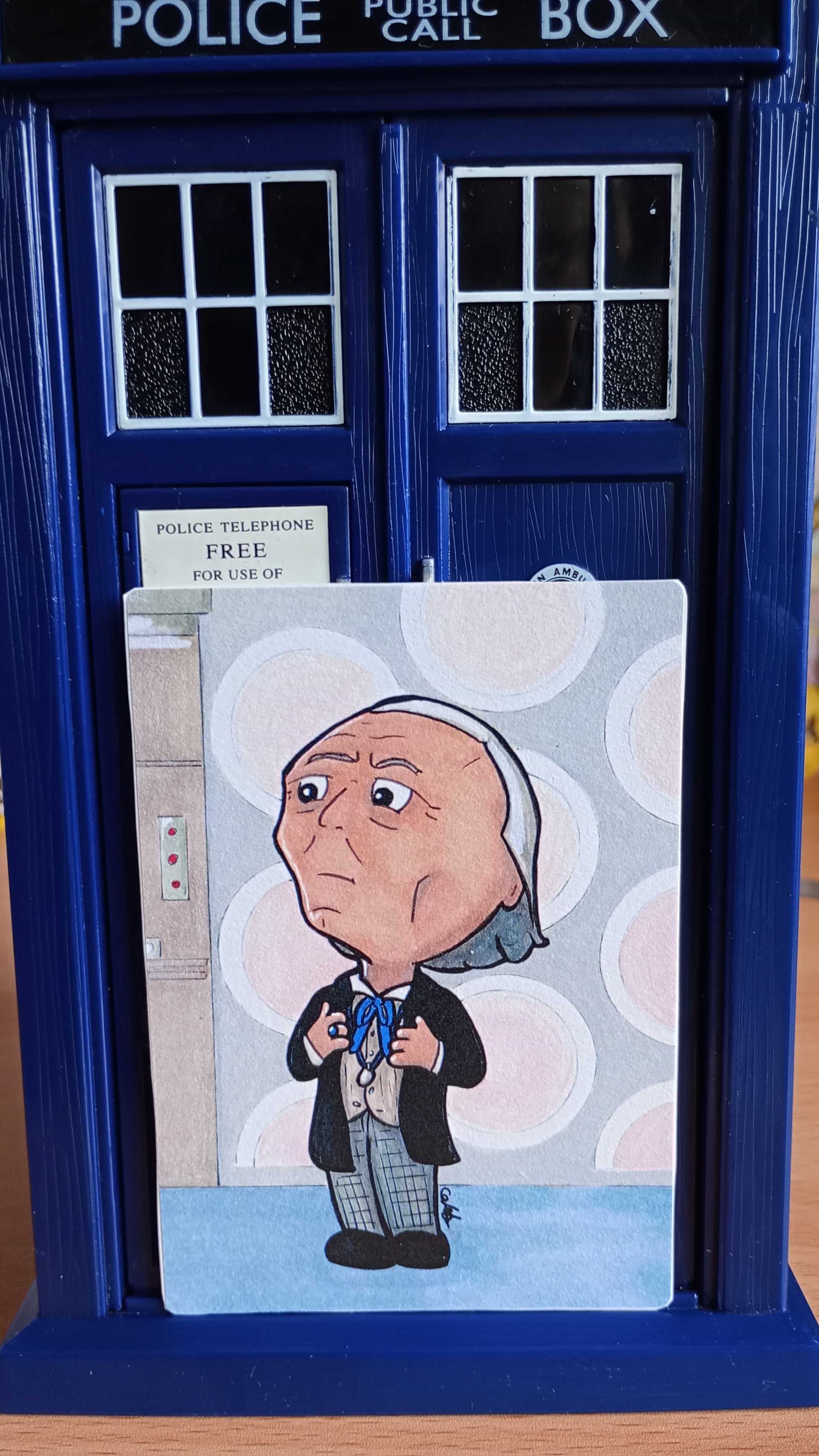 Large rectangular sticker with a picture of a Chibi Doctor Who drawing, set in front of a toy TARDIS 